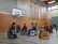 Das Bild zeigt mehrere Rollstuhlfahrer in der Turnhalle, die Wheelsoccer spielen.